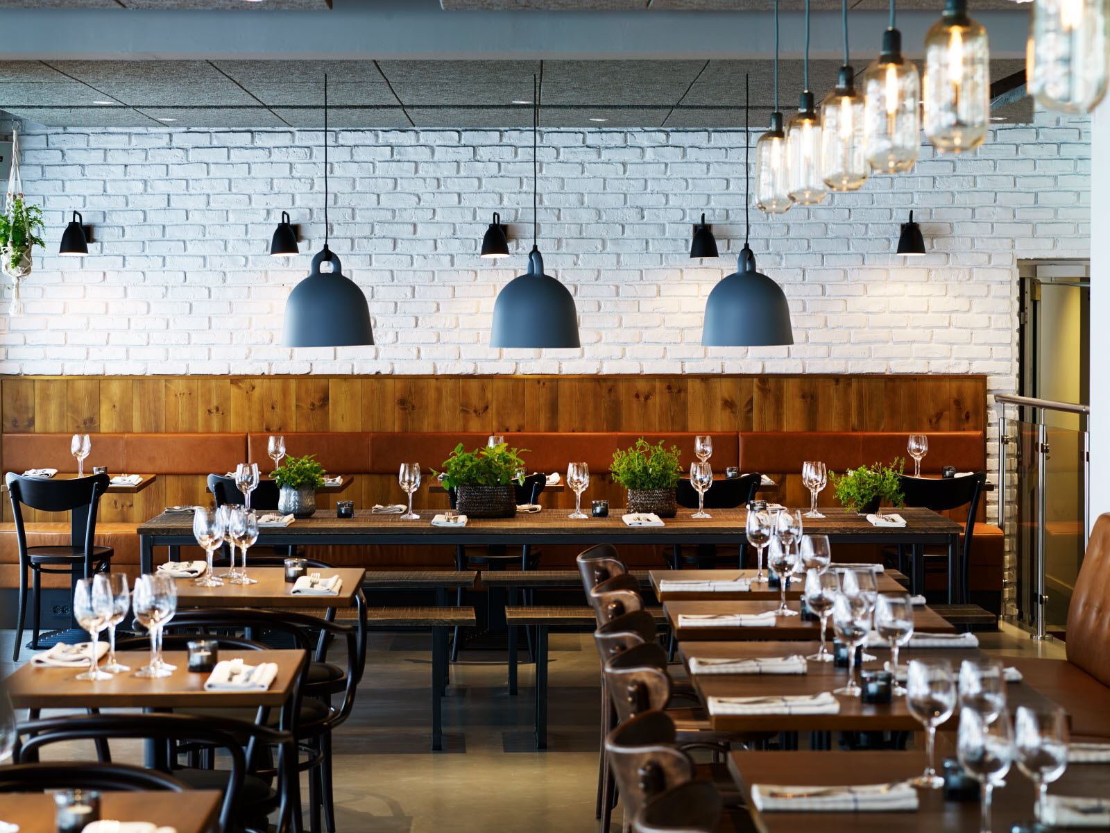 Modern looking restaurant or food facility with white subway tile on back wall, high seats & tables.