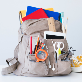 A tan backpack overflows with schools supplies.