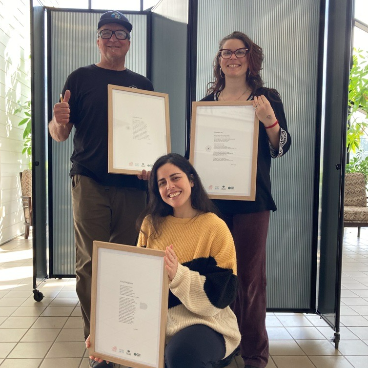 Three people stand in the Rood center lobby holding framed poems