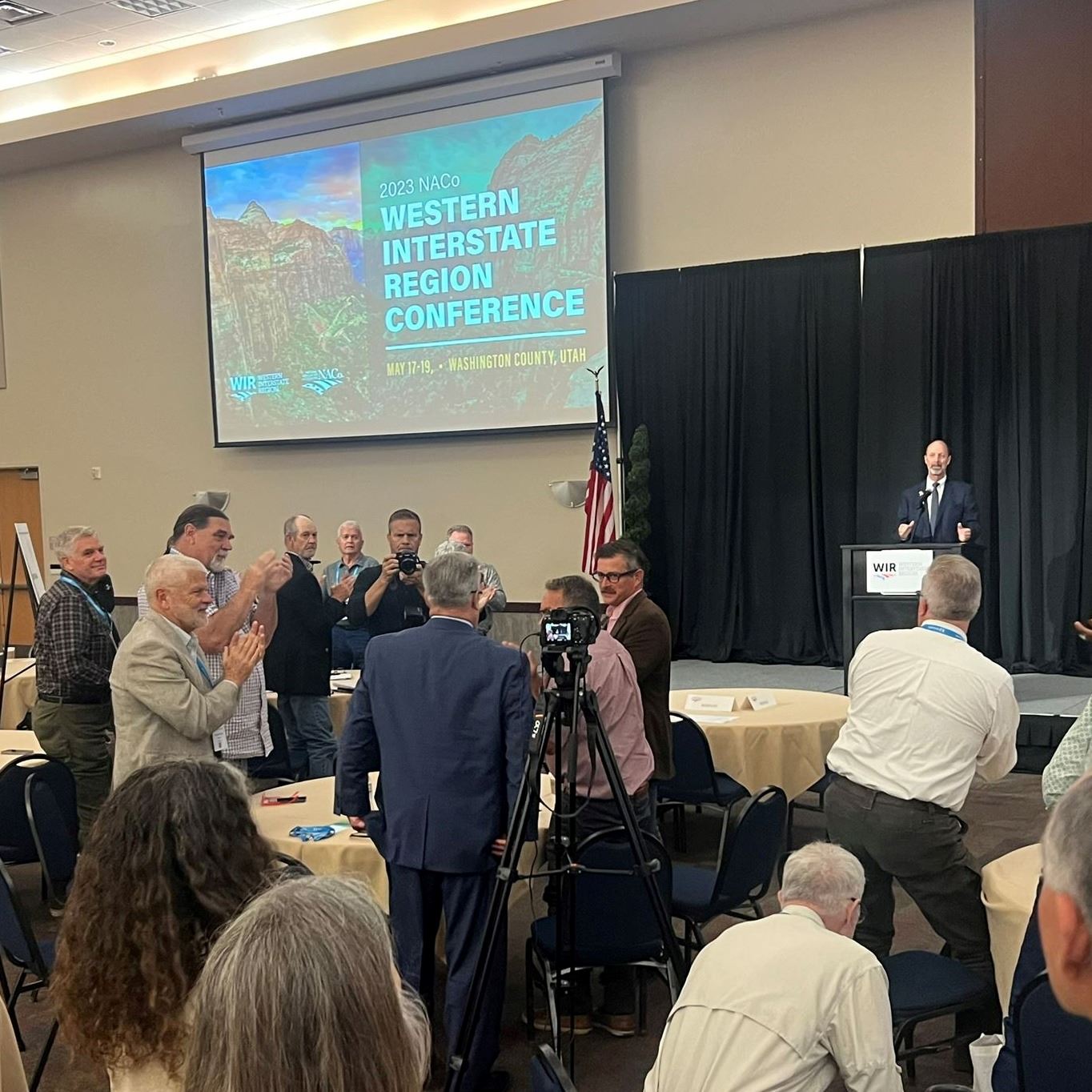 A group of people in a hotel conference room clap for the speaker onstage