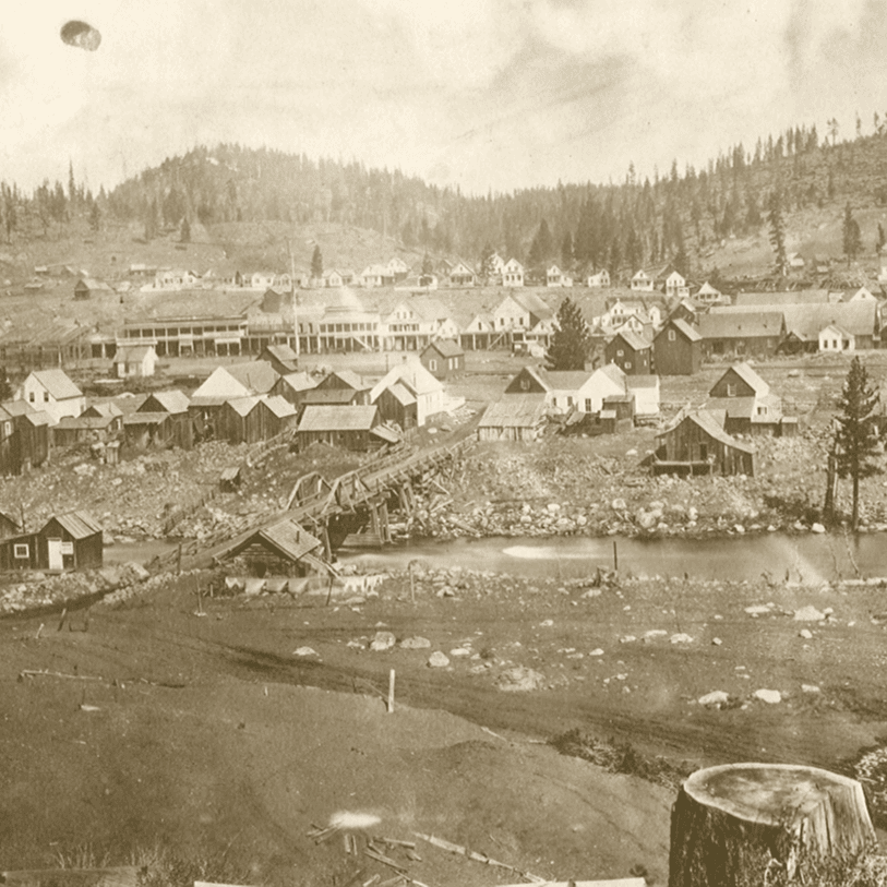 Sepia toned photograph of small wooden buildings along a river