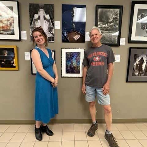 Two people stand smiling in front of a photography exhibit