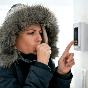 A person wearing a heavy winter coat with fur lining adjusts a thermostat