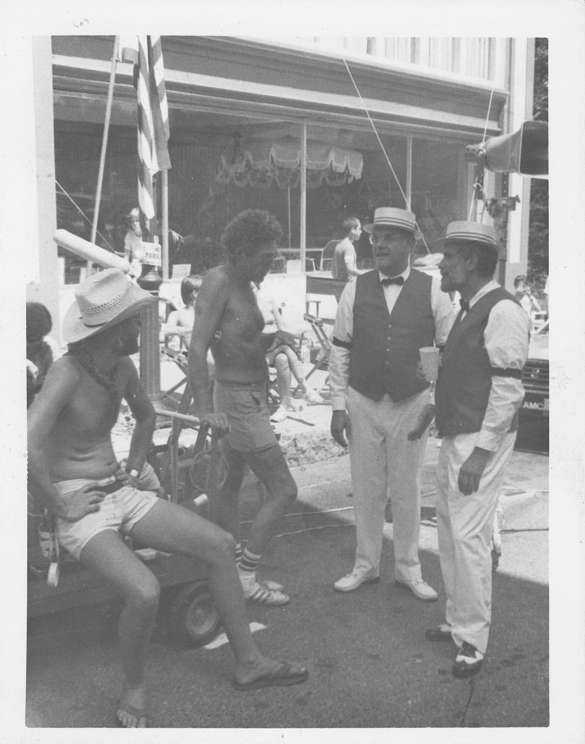 four men, two without shirts, talk with two men in formal attire