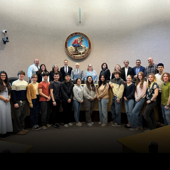 a large group of youth pose in the board chambers alongside board of supervisors