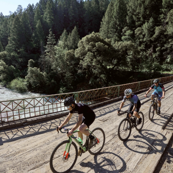Bike riders travel across a bridge and river