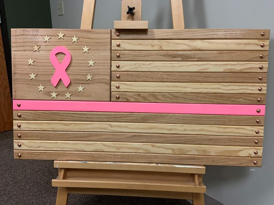 A handmade wooden flag with a pink stripe and a pink ribbon rests on an easel.