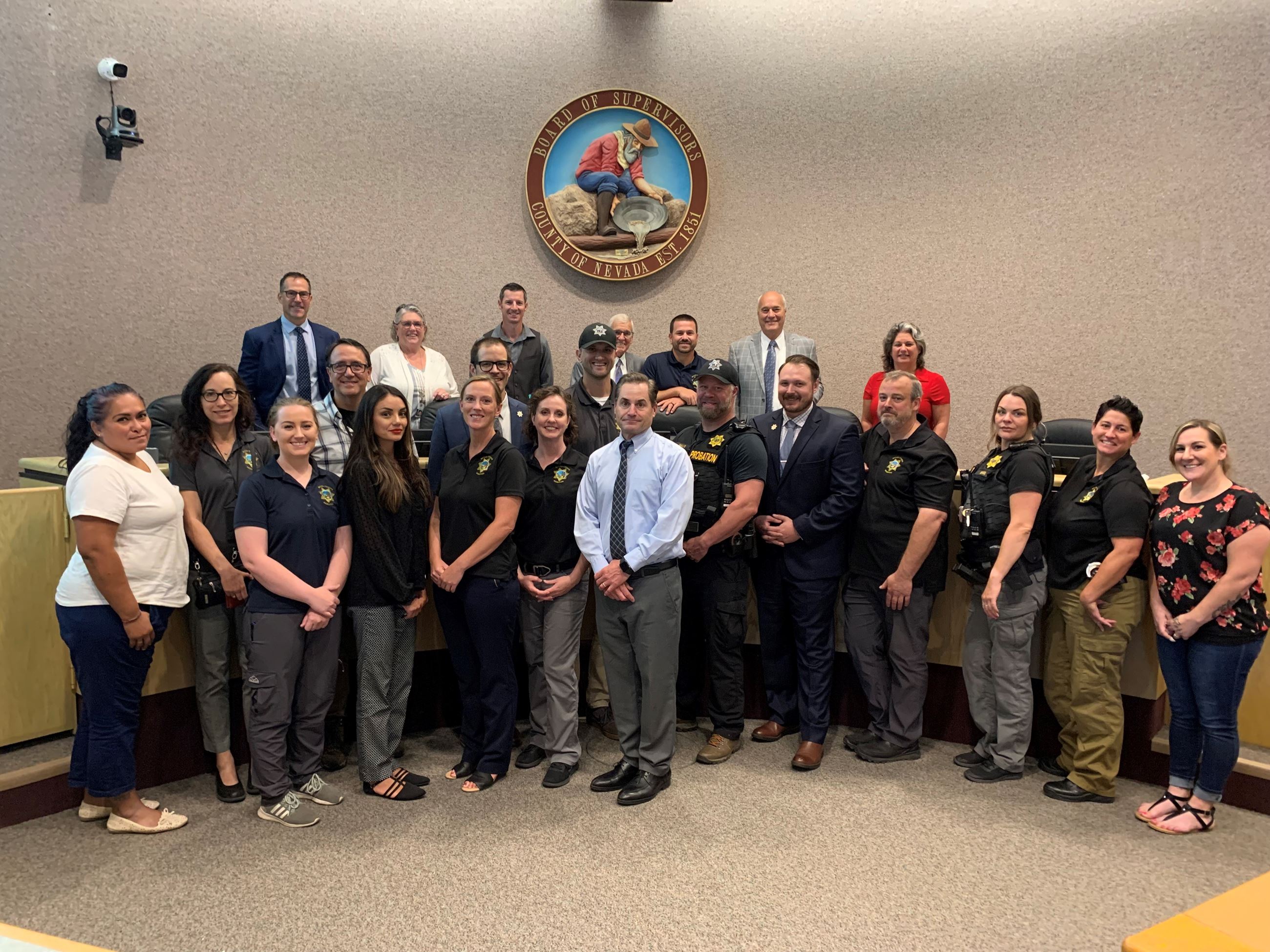 A large group of people pose on and in front of the Nevada County Board of Supervisors' dais.
